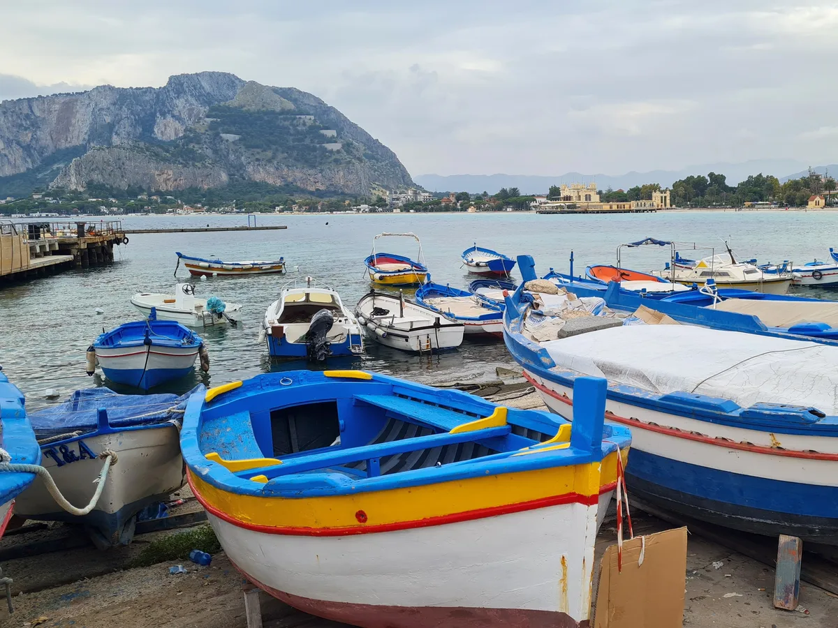 Brightly painted wooden fishing boats pulled up on the shore at Mondello with the mountain behind.