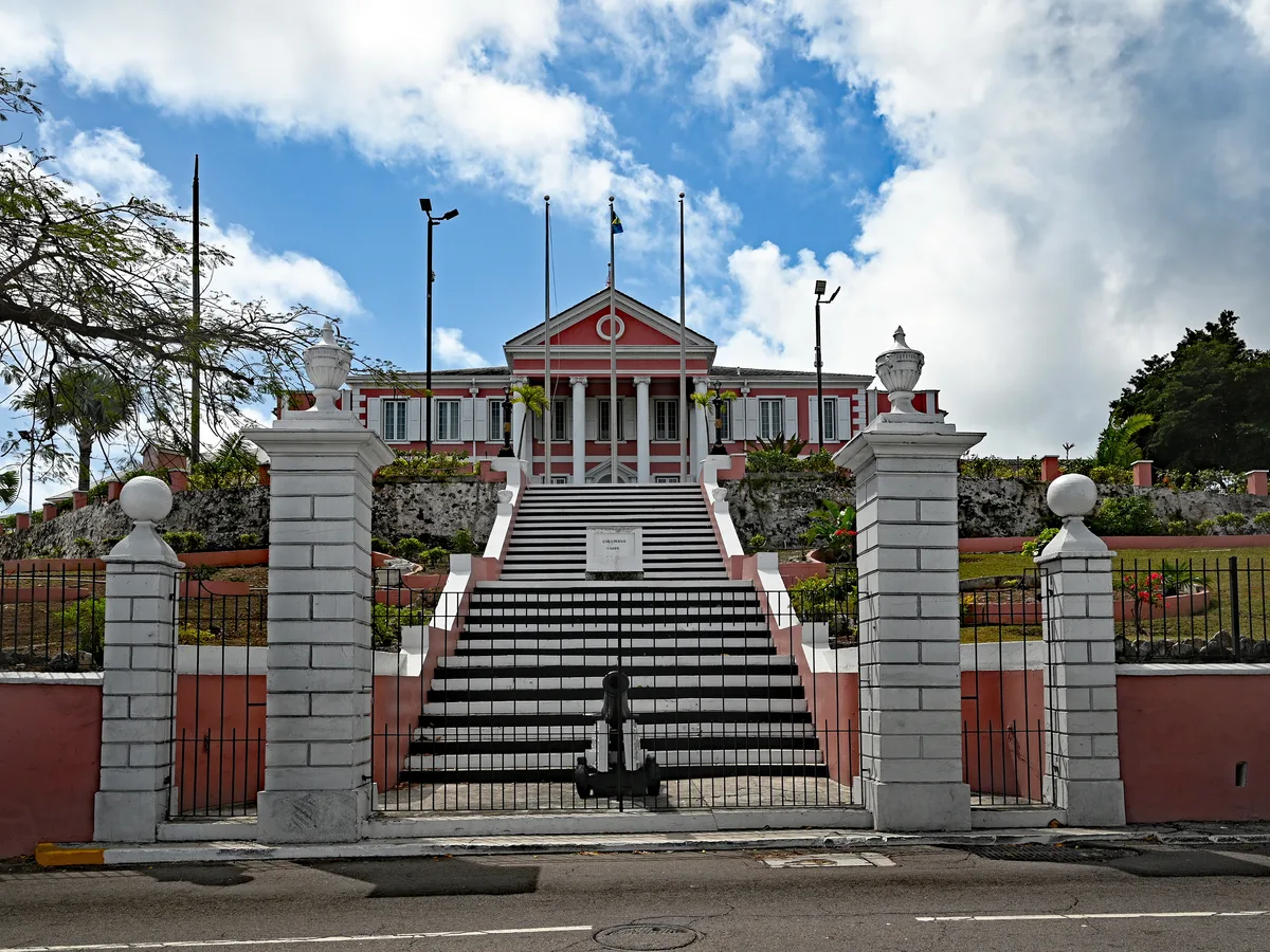 The red and white Government House atop a wide black and white staircase behind iron gates in Nassau.