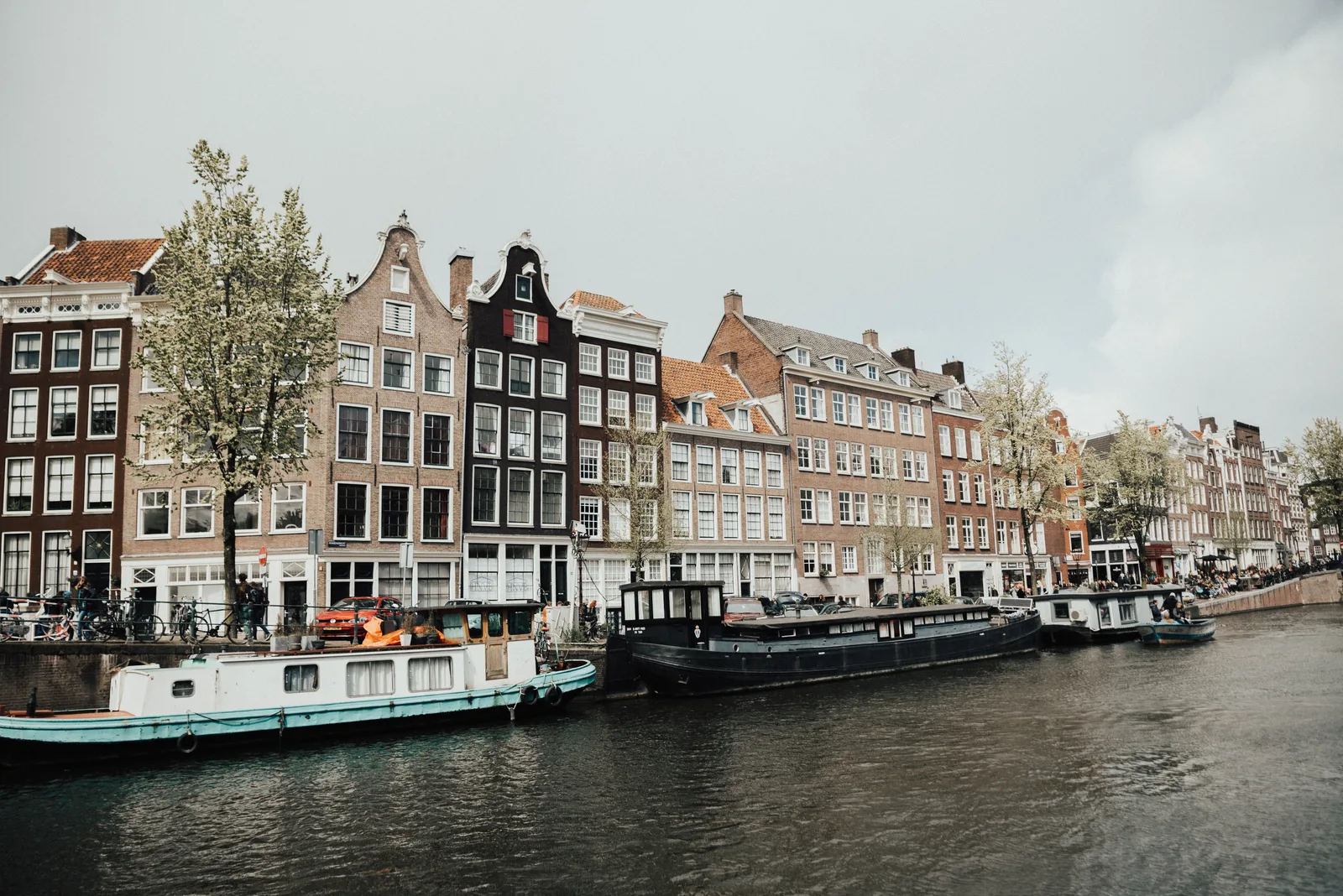 A row of narrow gabled canal houses reflected in an Amsterdam canal with houseboats moored in front.