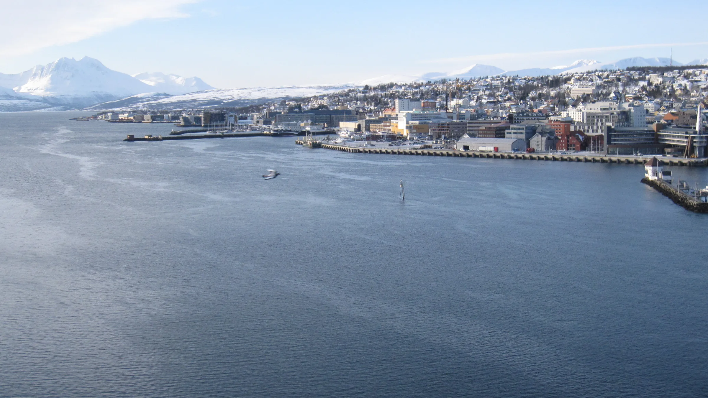 Tromso seen from the Tromso Bridge across the Tromsoysundet strait with snow-capped peaks on the far horizon.