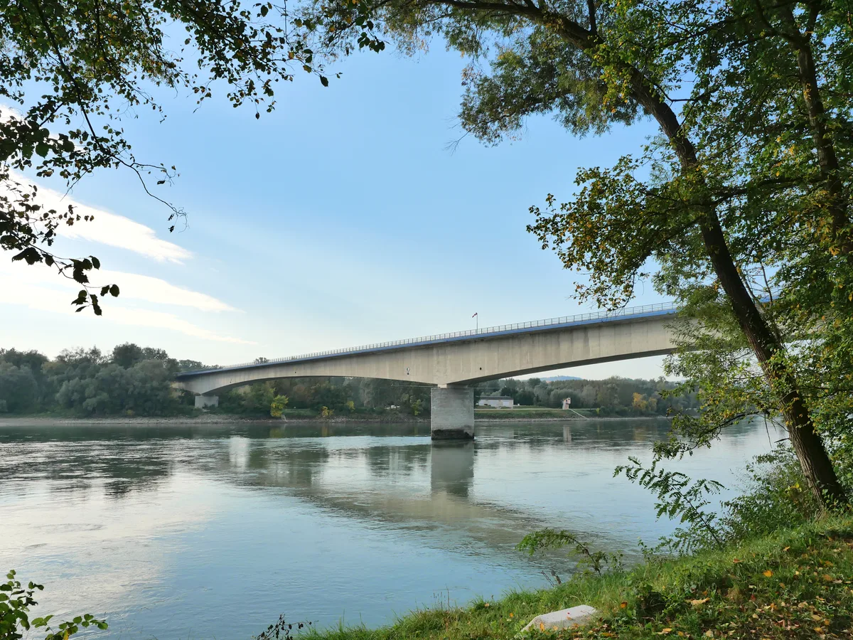 A modern concrete road bridge over the Danube at Melk seen from the grassy bank on a calm morning.