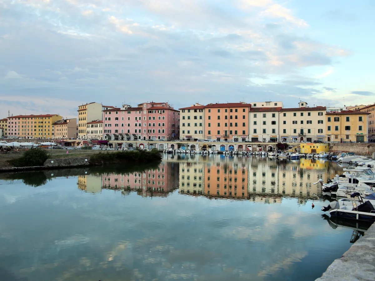 Pastel waterfront houses along the Scali delle Cantine canal in Livorno, reflected in still water.