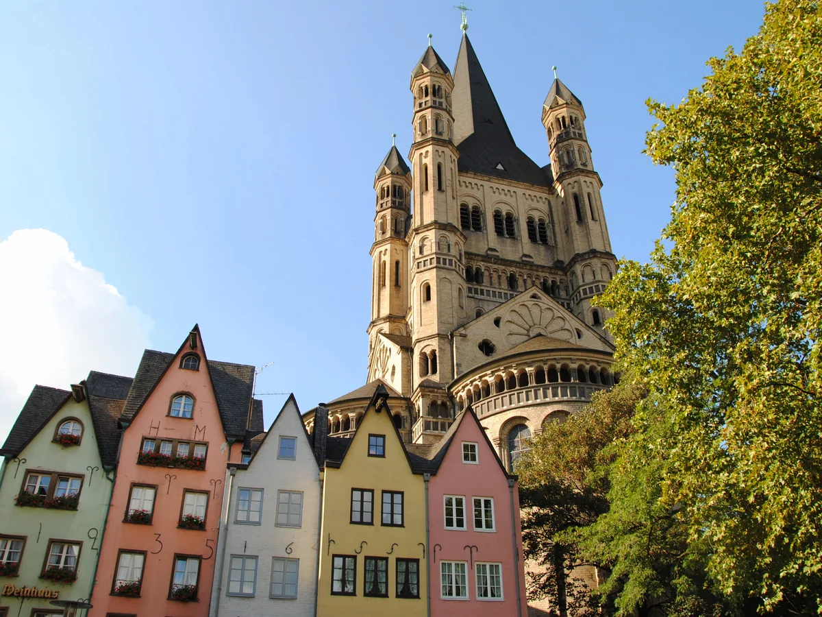 The tower of Groß St. Martin rising above the pastel gabled houses of the Fischmarkt on a sunny day in Cologne.