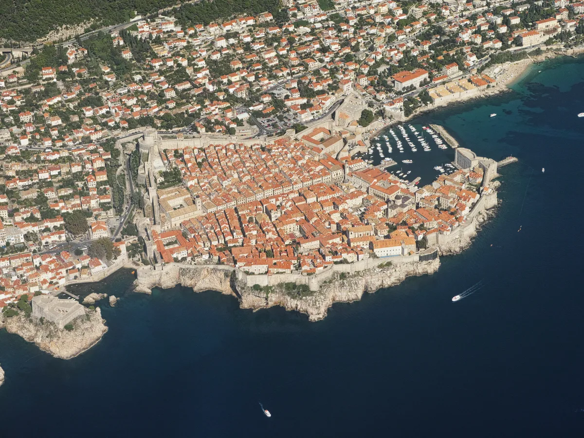 Aerial view of Dubrovnik's walled old town on its promontory with the harbour and the open sea beside it.
