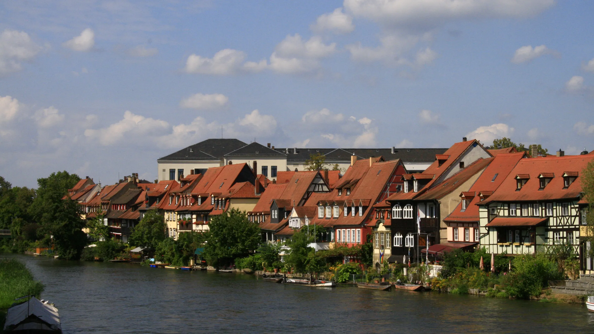Bamberg's Little Venice houses with orange roofs along the Regnitz under a blue sky with cumulus clouds.