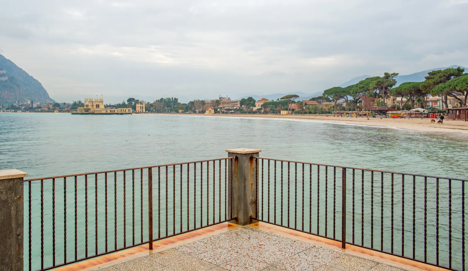 View across the bay of Mondello from a railed terrace, with the beach and bathing pavilion in the distance.