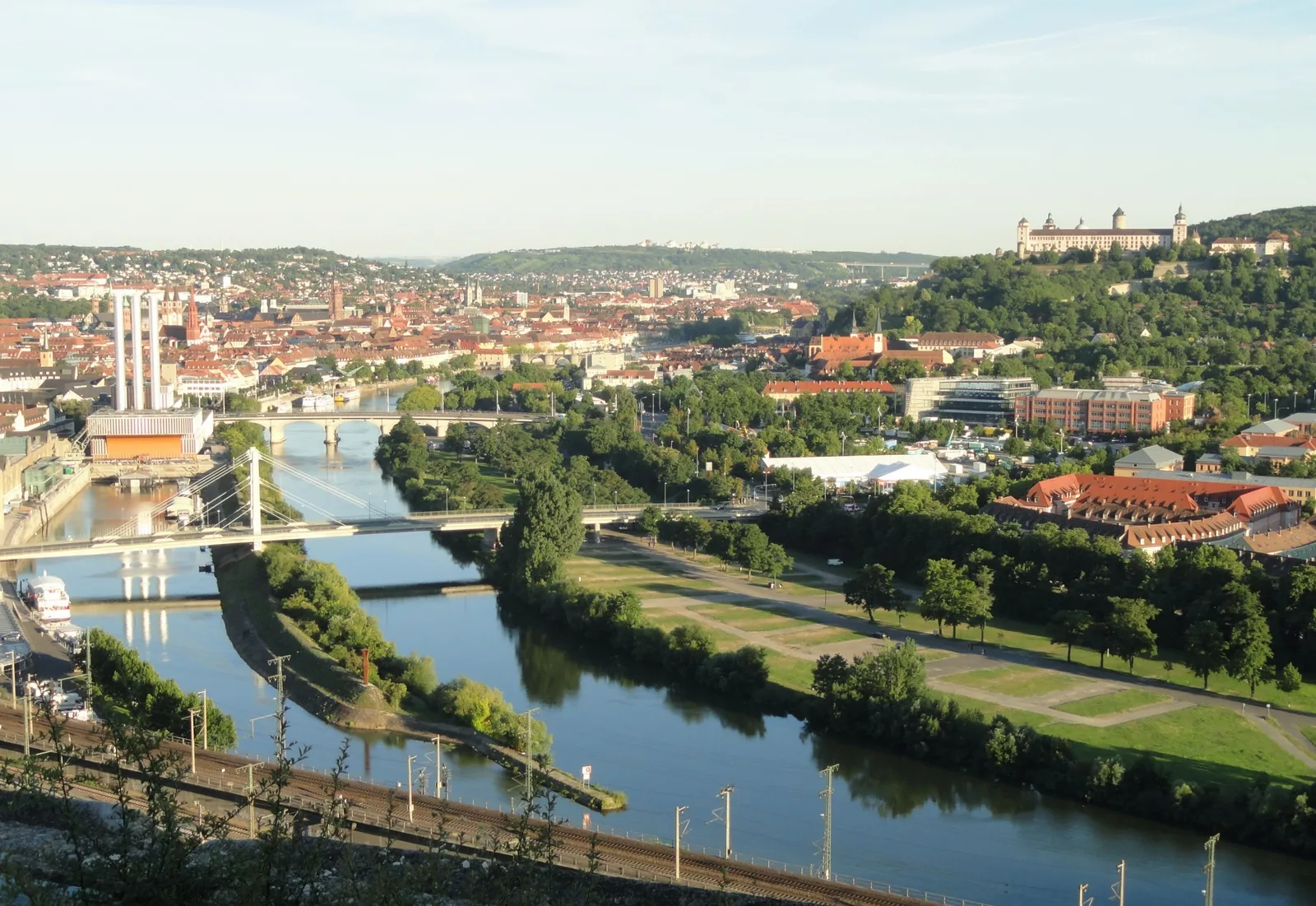 A panorama of Würzburg showing the red roofs of the old town, the Main river and the green riverbank beyond.