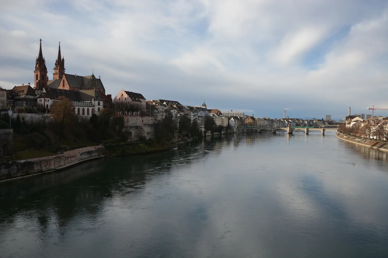 The Rhine flowing past the Basel old town toward the Münster, with scattered cloud above.