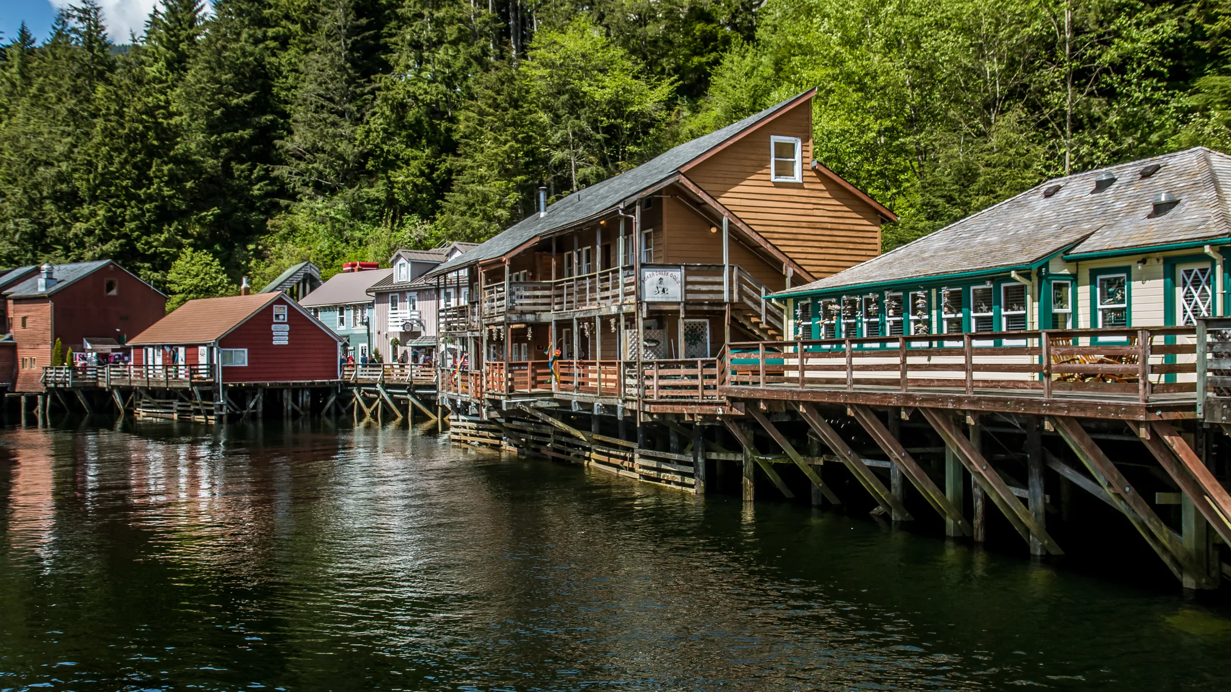 Wooden Creek Street buildings on stilts above the water, backed by evergreen forest.