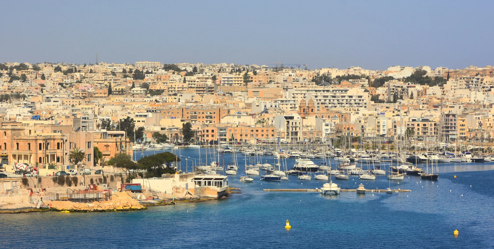 A marina crowded with boats and honey-coloured buildings on the far side of the harbour near Valletta.
