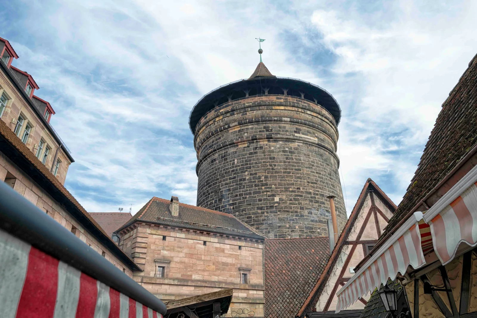 A round stone tower rising above half-timbered roofs and red and white market awnings in Nuremberg.