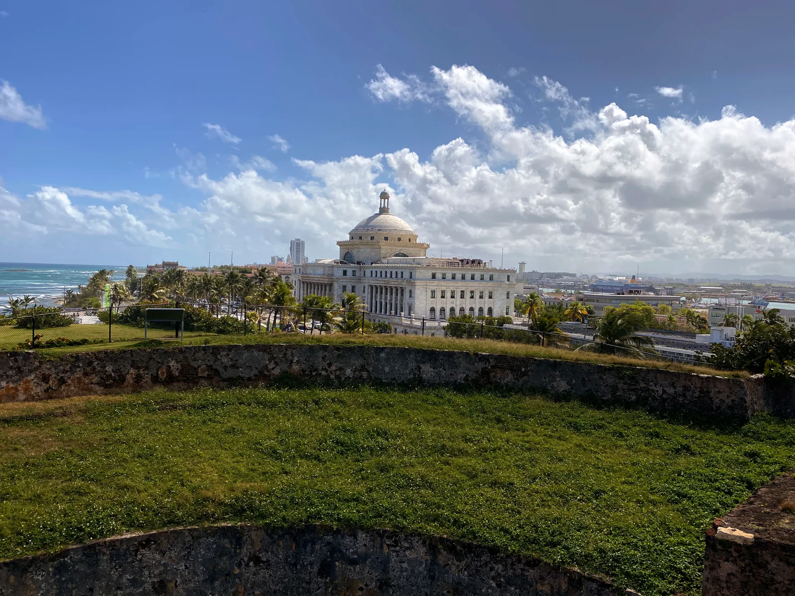 The white-domed Puerto Rico Capitol seen across a grassy fortress rampart from Castillo San Cristobal.