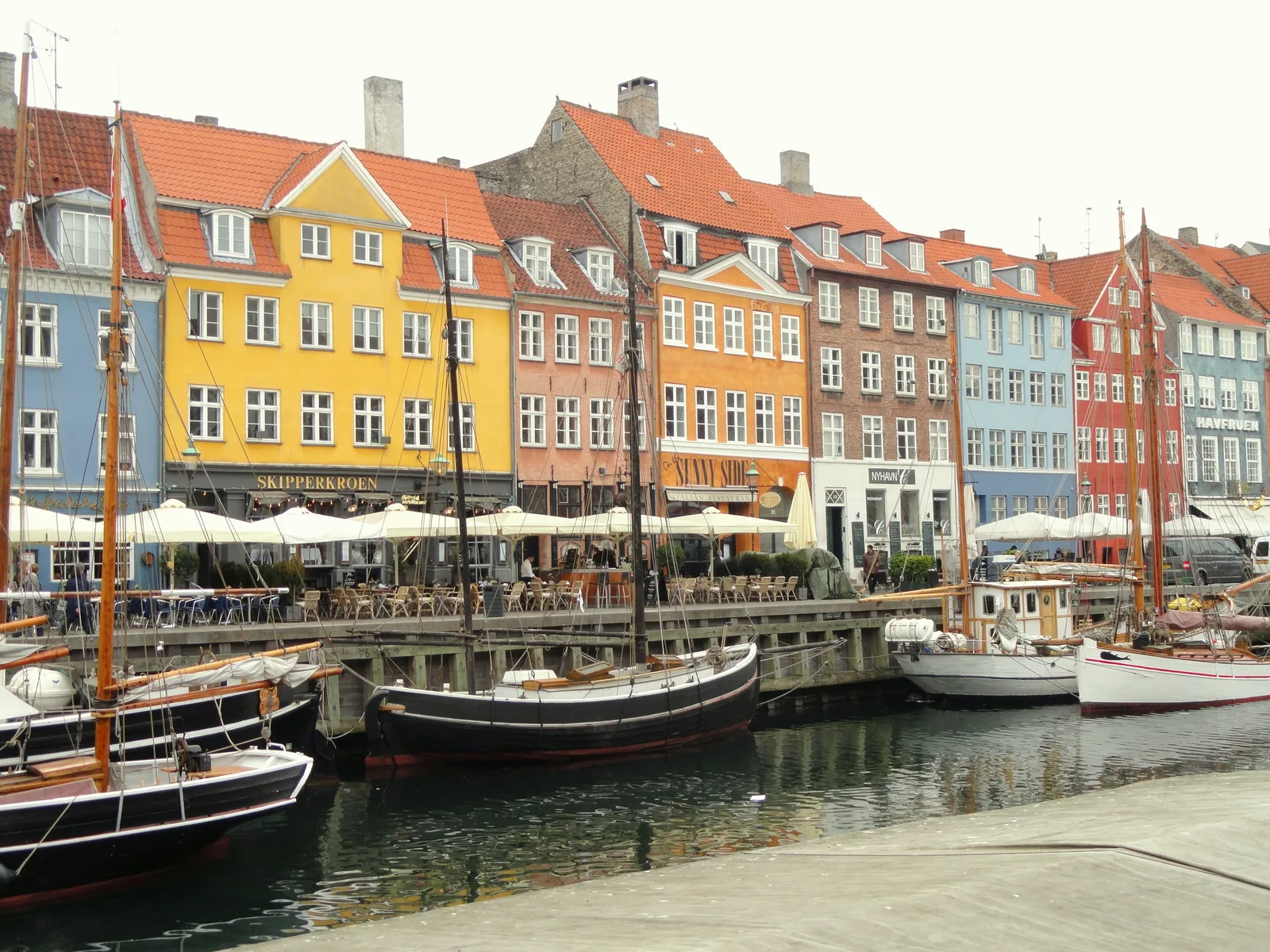 A sunlit row of Nyhavn houses behind moored sailing boats under white umbrellas.