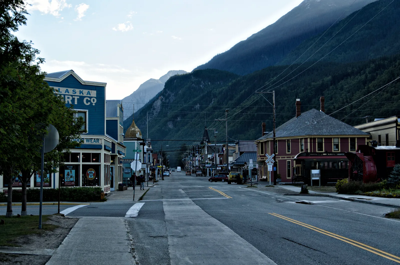 Broadway in Skagway looking up the street between historic storefronts, with a mountain slope rising on the right.