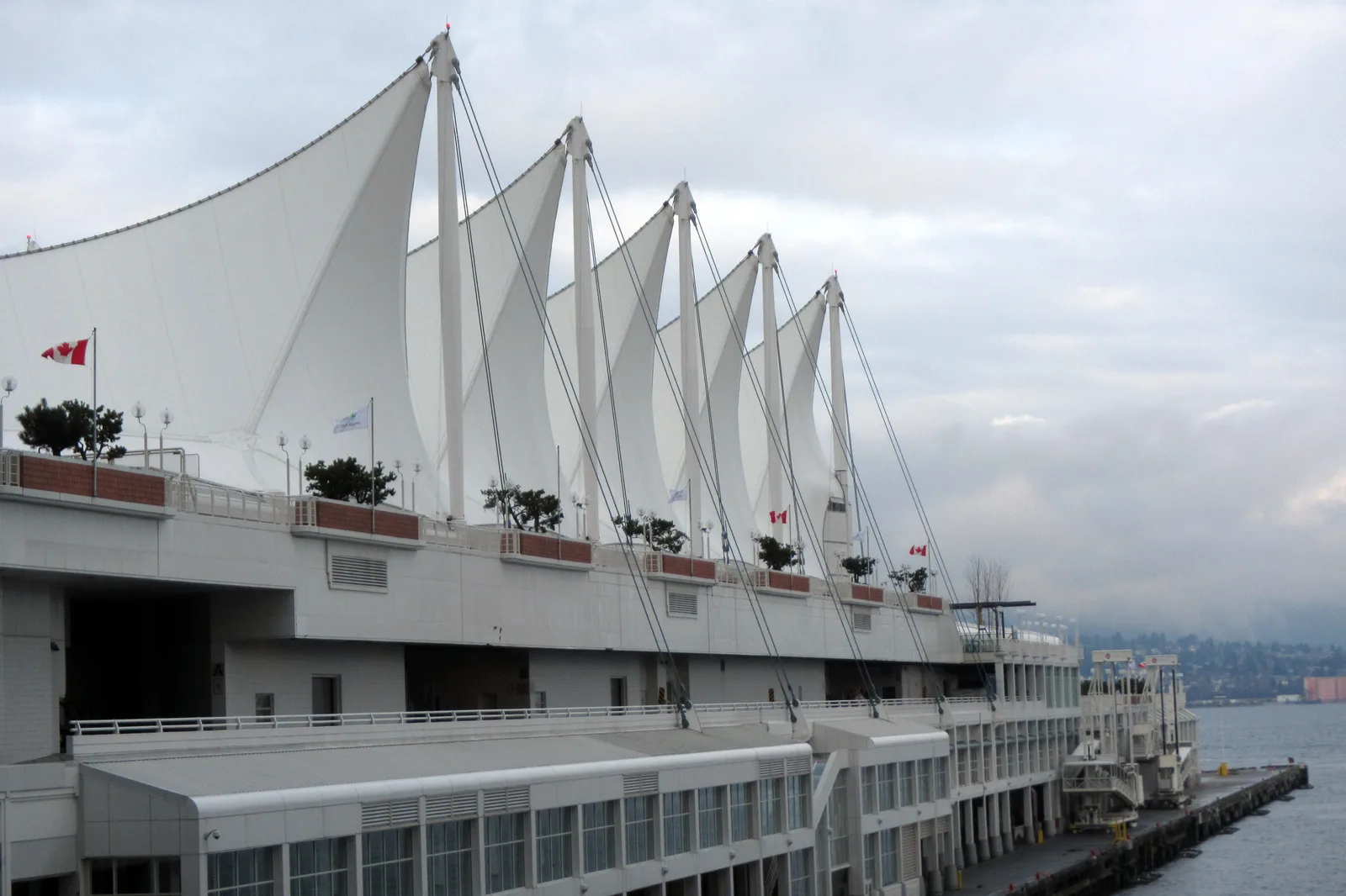 The white sails of Canada Place beside the harbour under an overcast sky with flags on the roof edge.