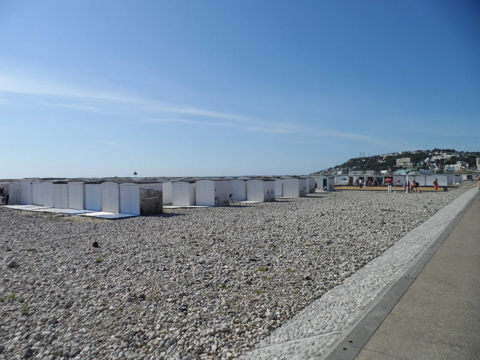 Rows of white beach huts on the Le Havre shingle beach with Sainte-Adresse on the hill behind.