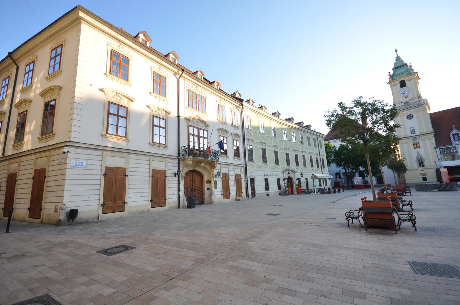 A pale yellow and green baroque building on the main square, with the old town hall tower at the side.