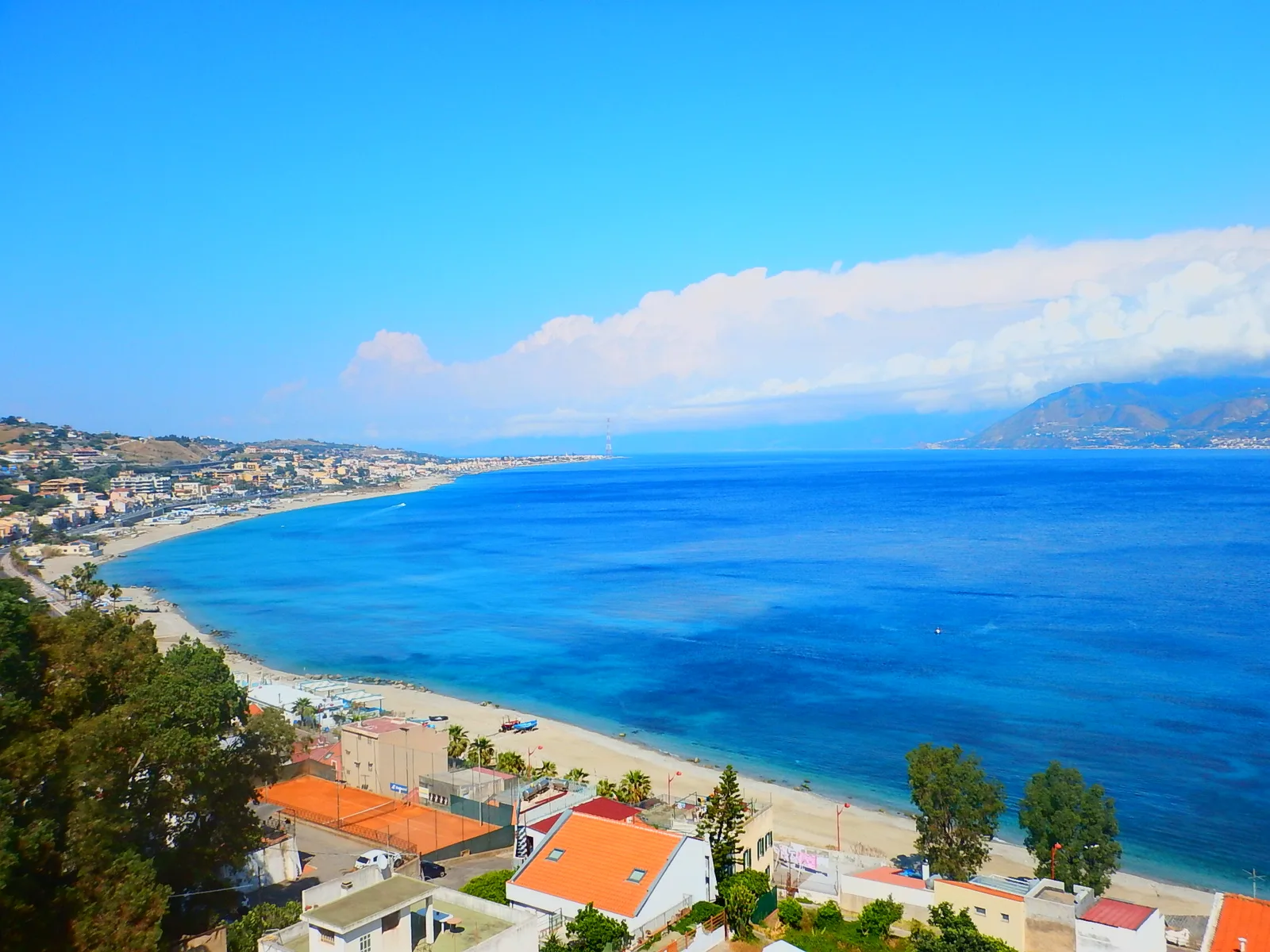 A blue sea and pebble beach on the Strait of Messina under a bright sky.