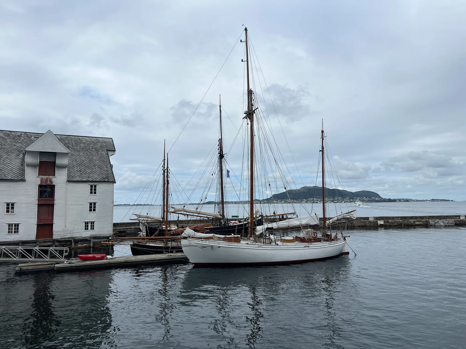 A white sailing boat moored by traditional timber warehouses on Alesund's harbour.