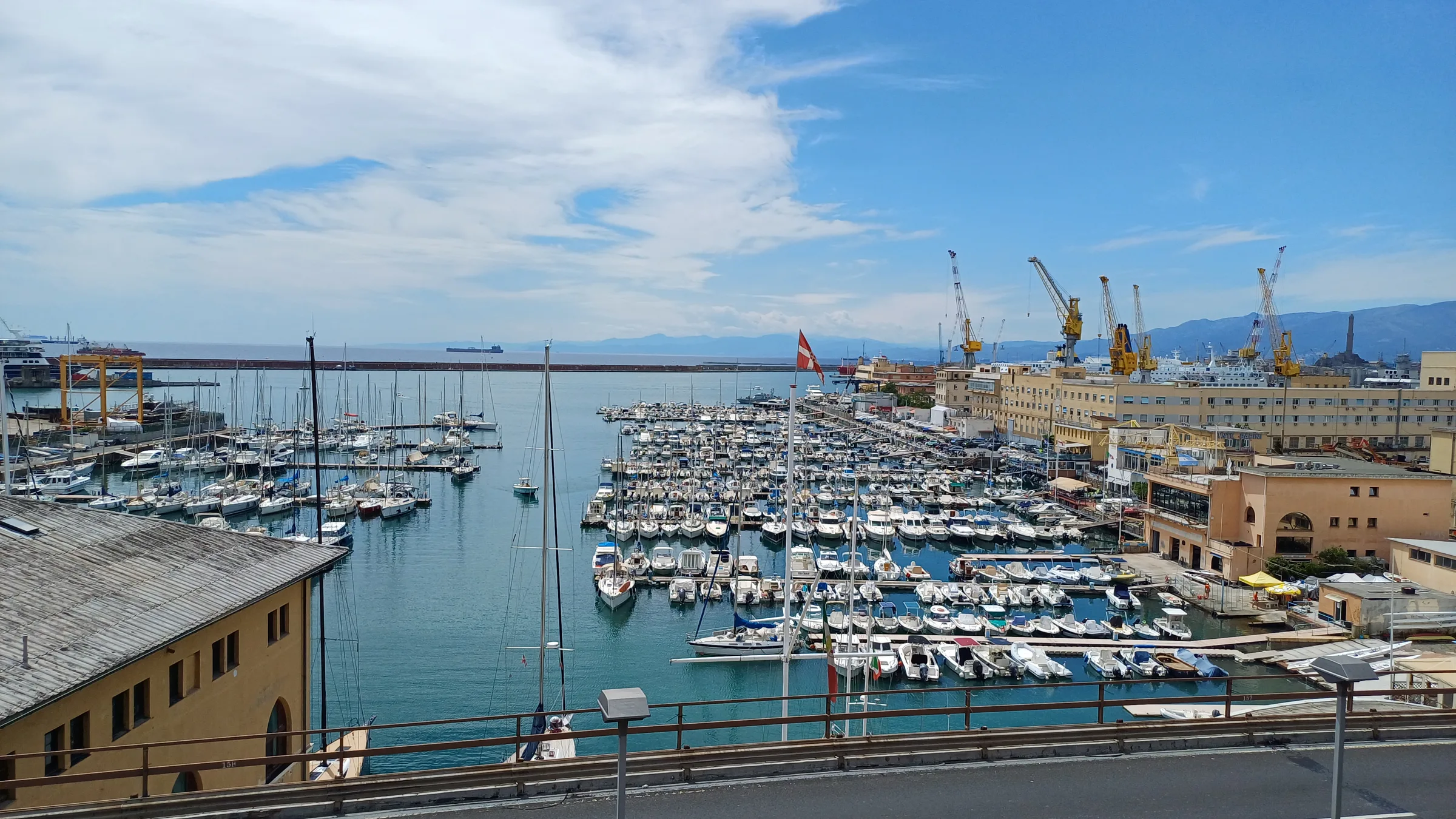 The Porticciolo Duca degli Abruzzi marina in Genoa full of moored boats, with harbour cranes beyond.