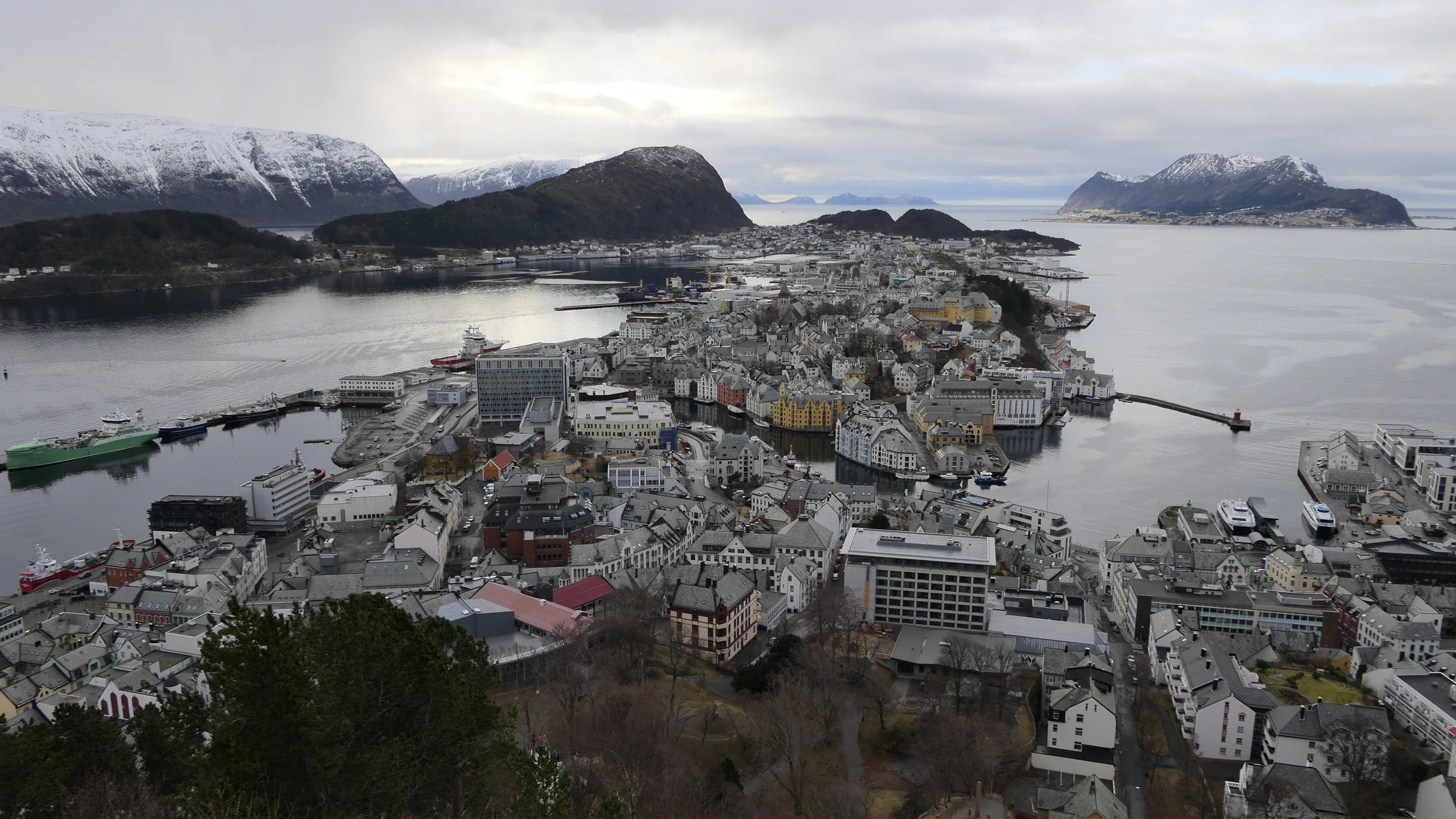 An elevated view over Alesund's town island, harbour and fjord with snow-topped peaks in the distance.