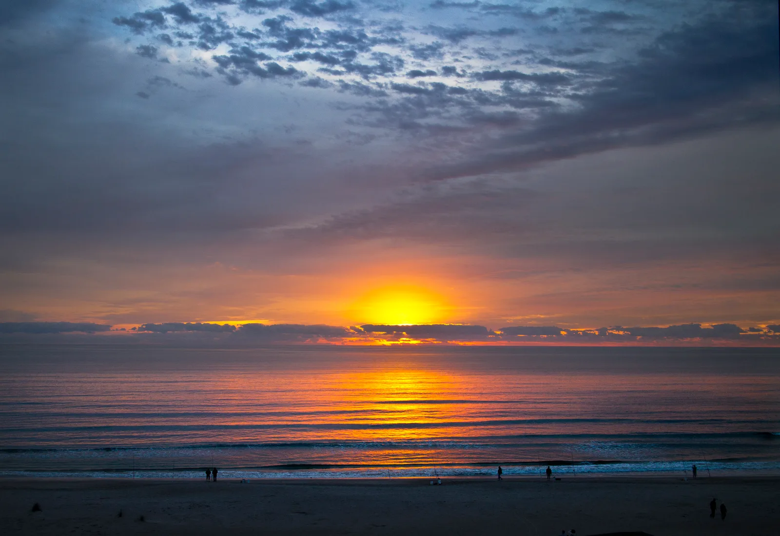 The sun rising over the Atlantic at Cocoa Beach, with cloud bands in the sky and a dark foreground beach.