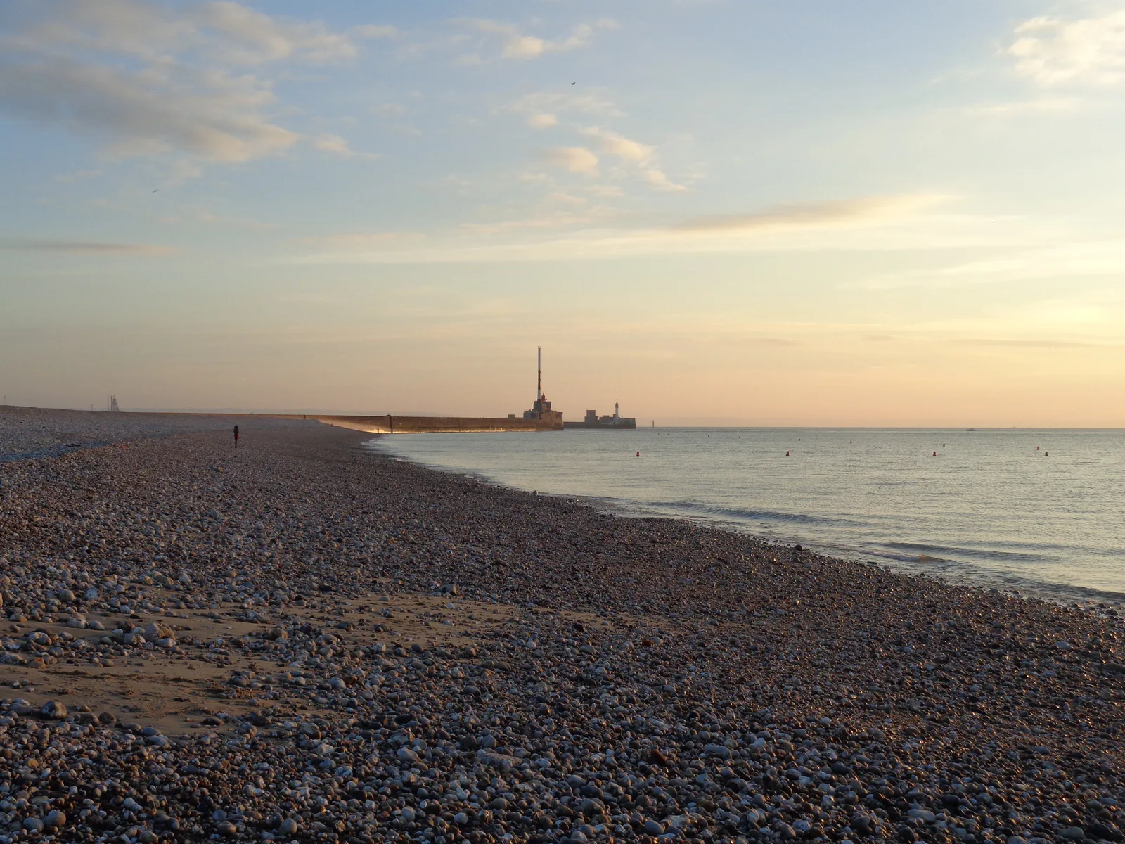 The shingle beach at Le Havre curving toward the pier under an evening sky.