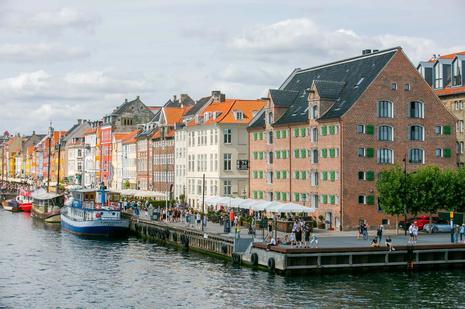 Nyhavn's pastel facades with cafe umbrellas along the quay and a tour boat on the water in Copenhagen.