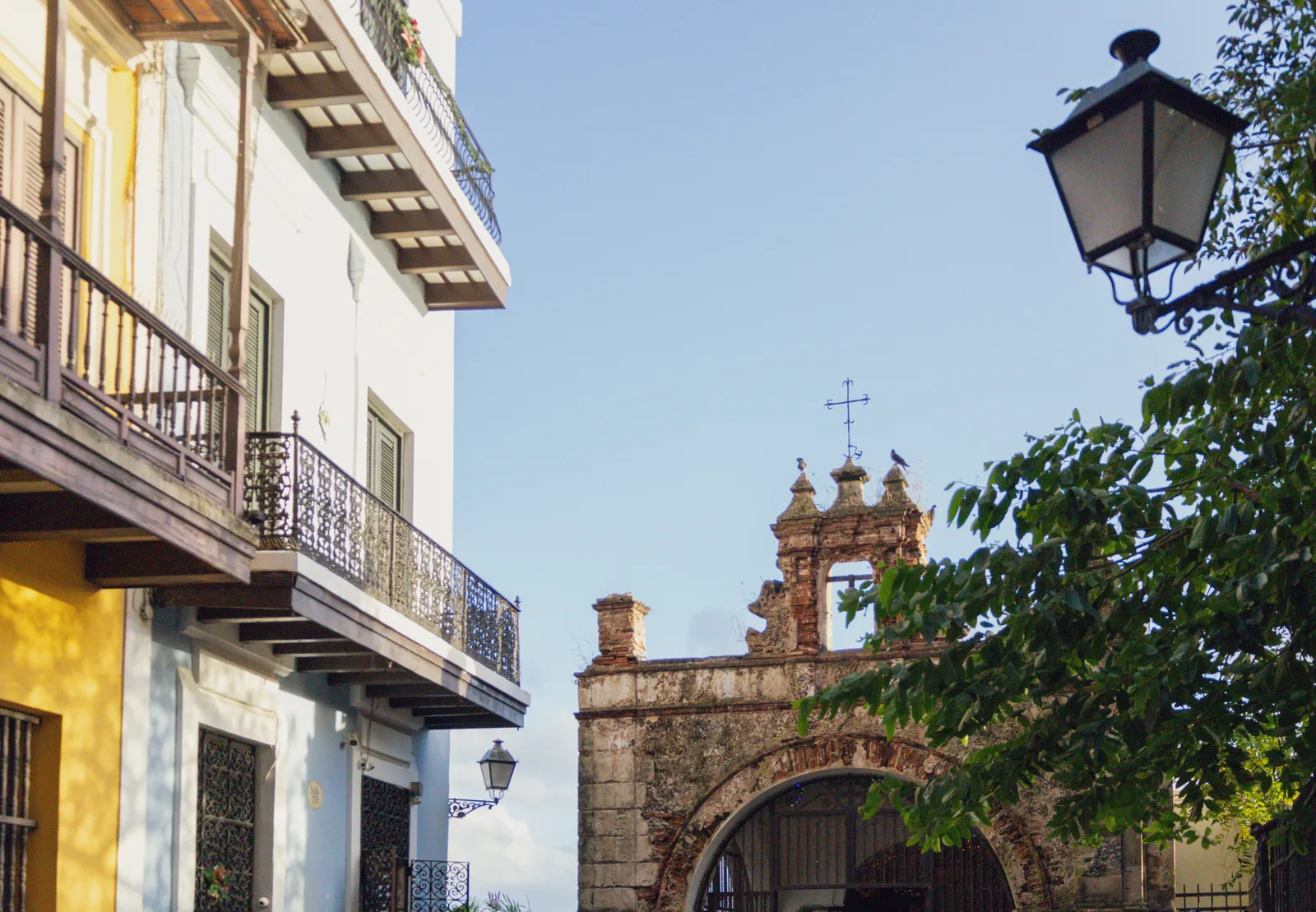 A balconied yellow building and a stone chapel beside a street lamp on Calle del Cristo in Old San Juan.