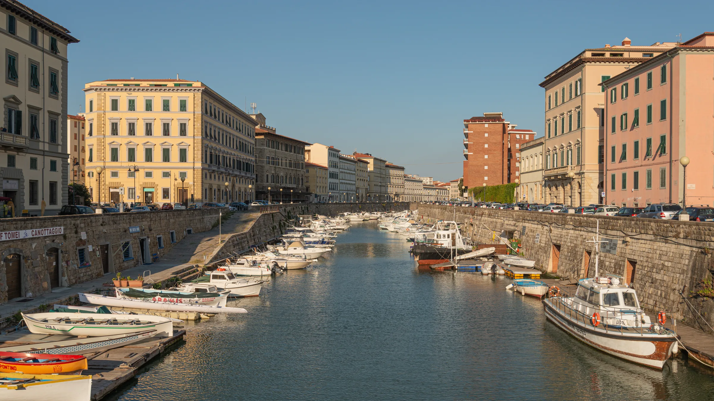 Boats moored along the Fosso Reale canal in Livorno, lined with colourful townhouses at golden hour.