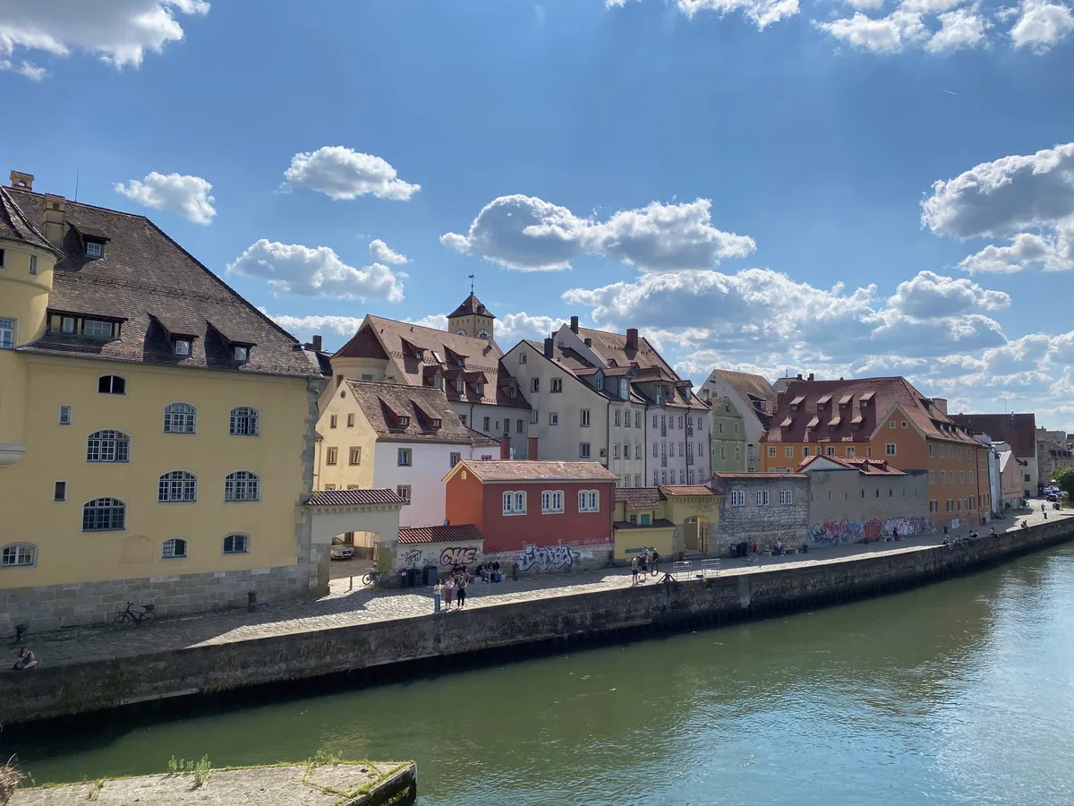 Pastel houses along a quay on the Danube bank in Regensburg under a blue sky.