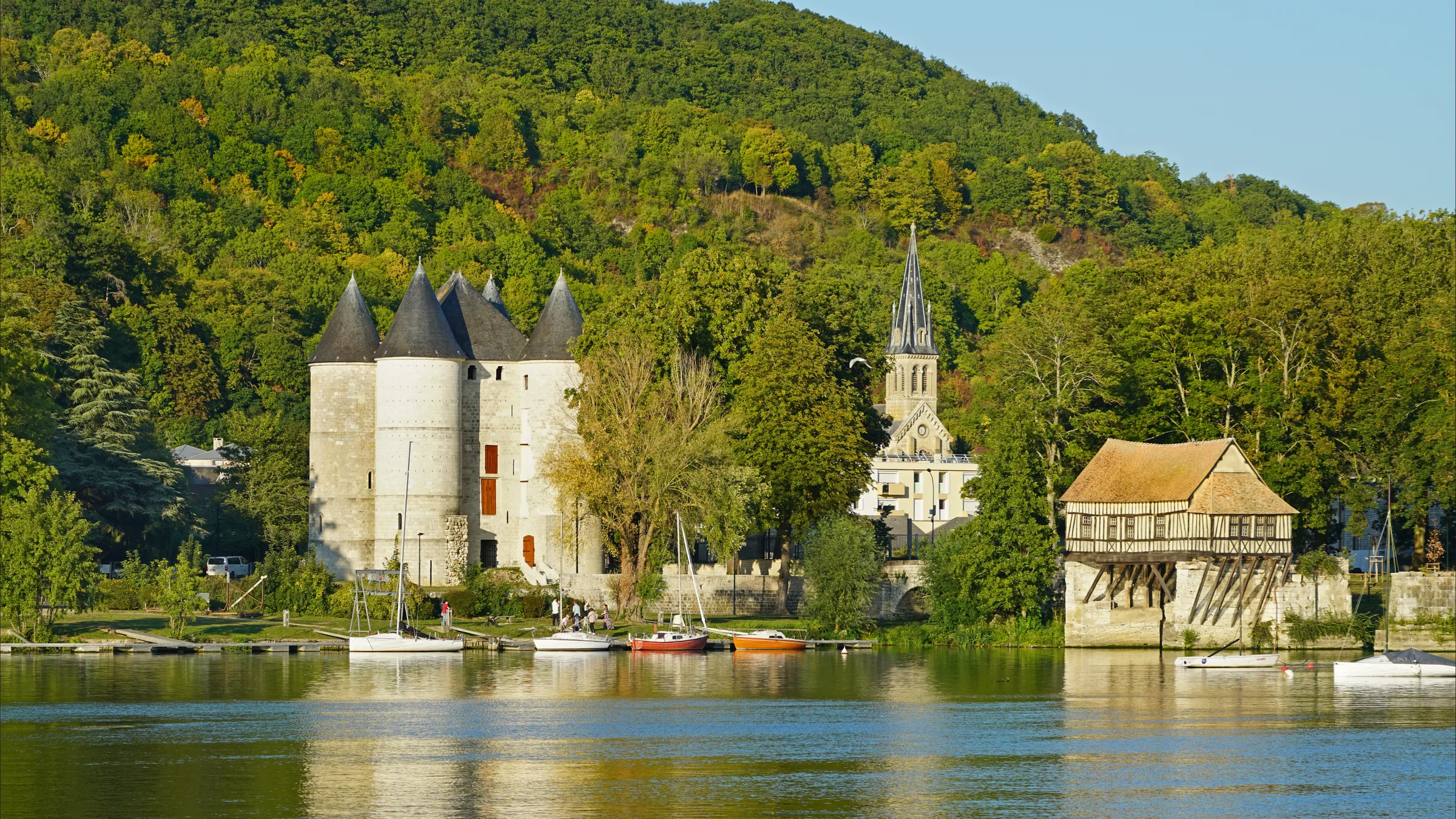 The round towers of the Château des Tourelles and the timbered Vieux Moulin on the Seine at Vernon, with a wooded hill behind.