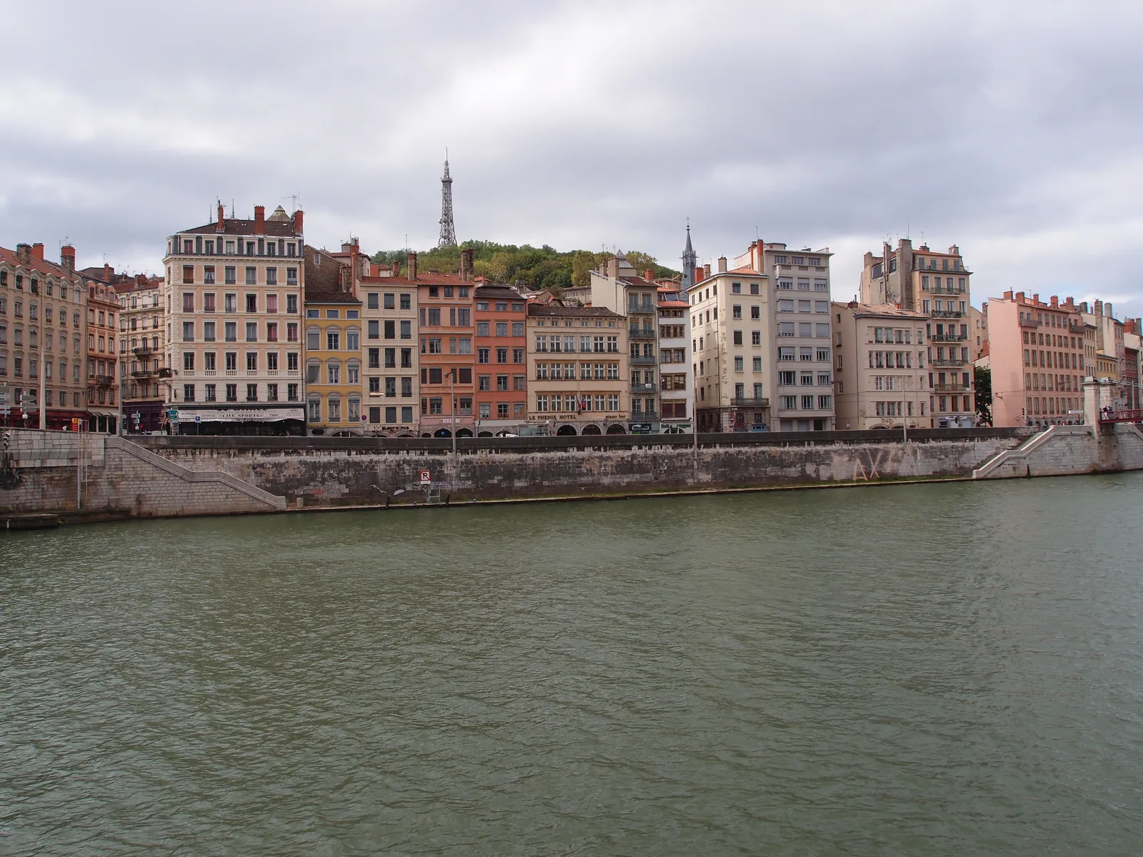 Colourful houses along the Saône with a tower above them on the Fourvière hill, seen across the water.