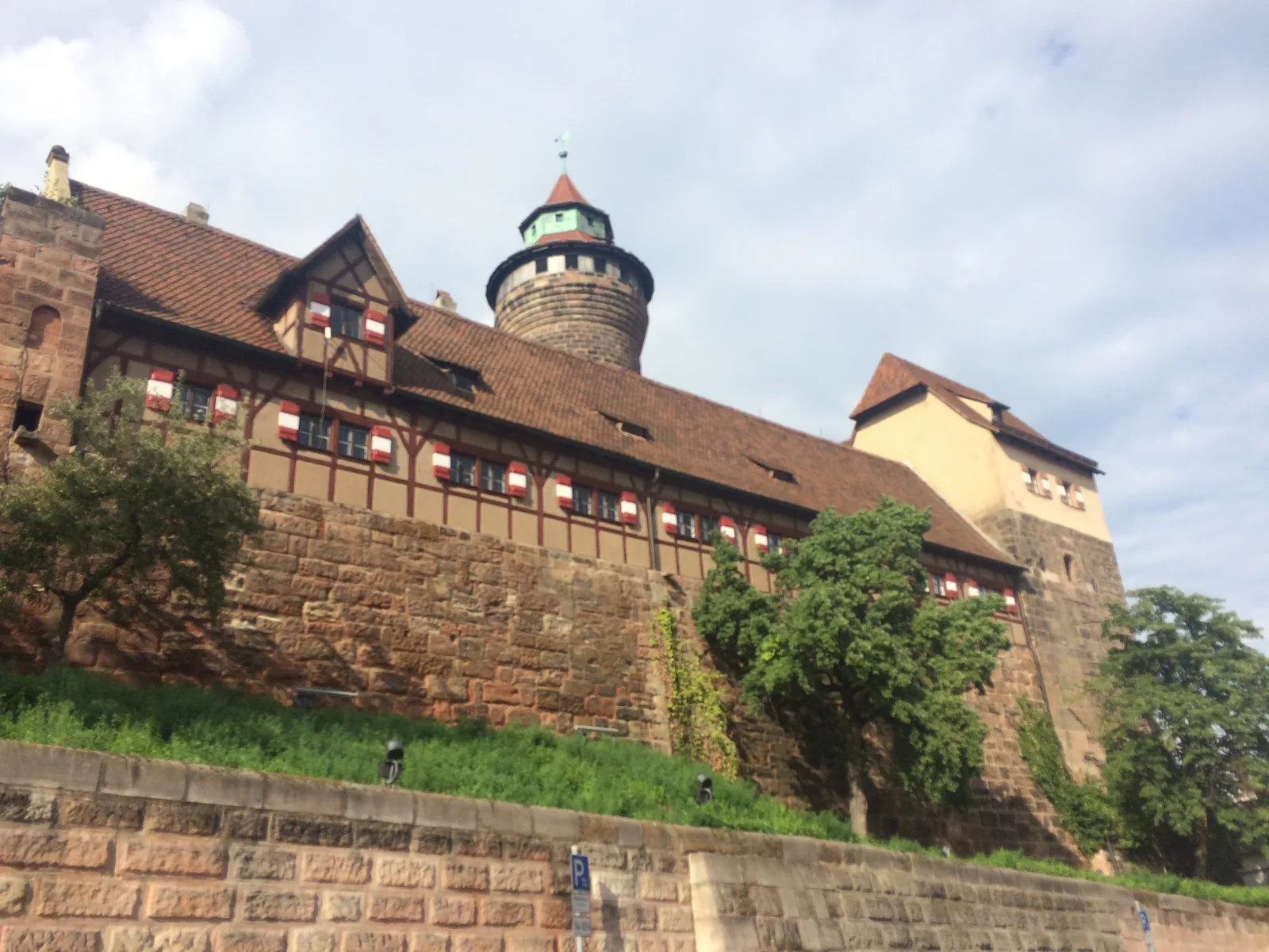 A sandstone castle wall and a round tower above a grassy slope in Nuremberg.