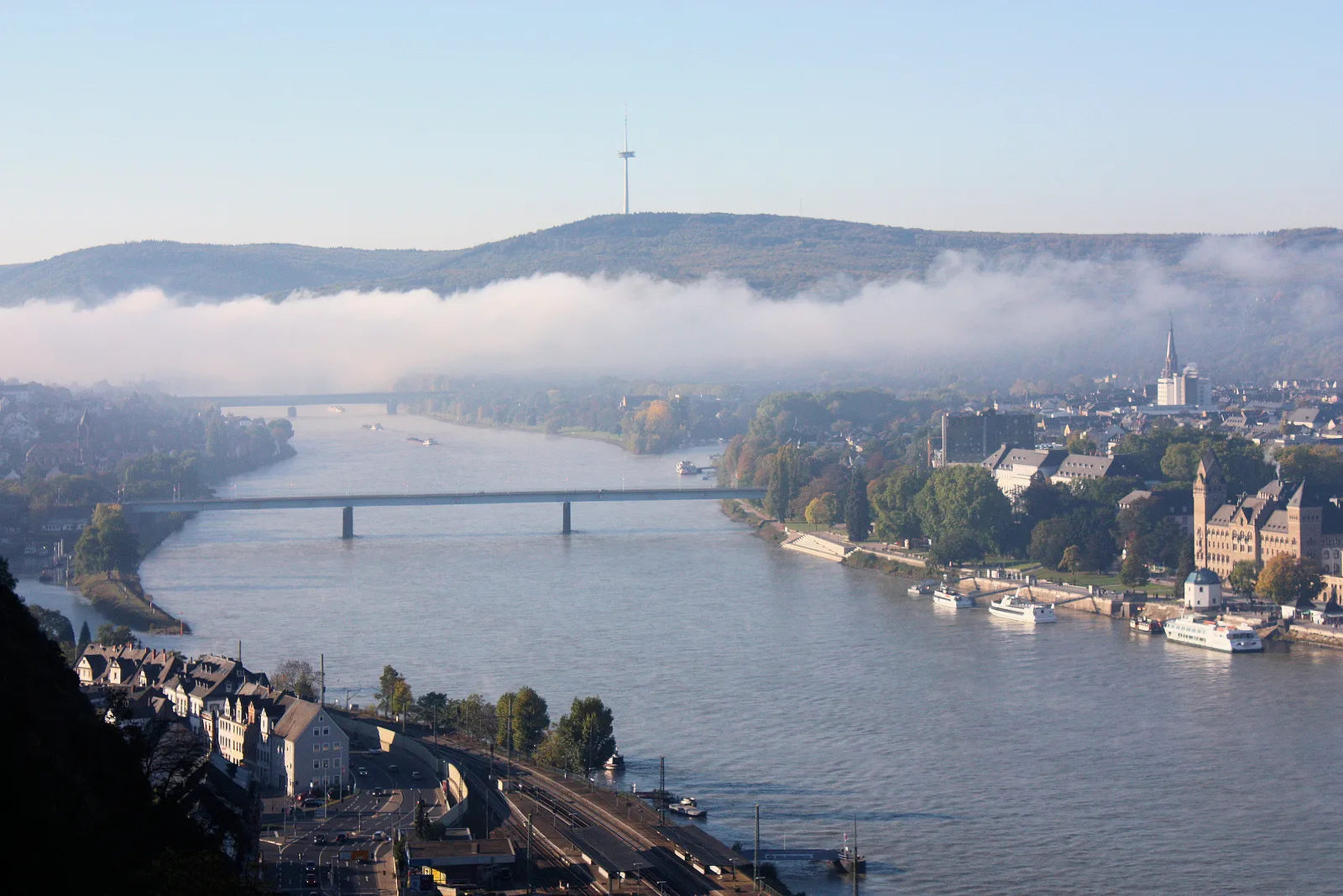 The Rhine curving past Koblenz under a low mist, with a wooded hill behind.
