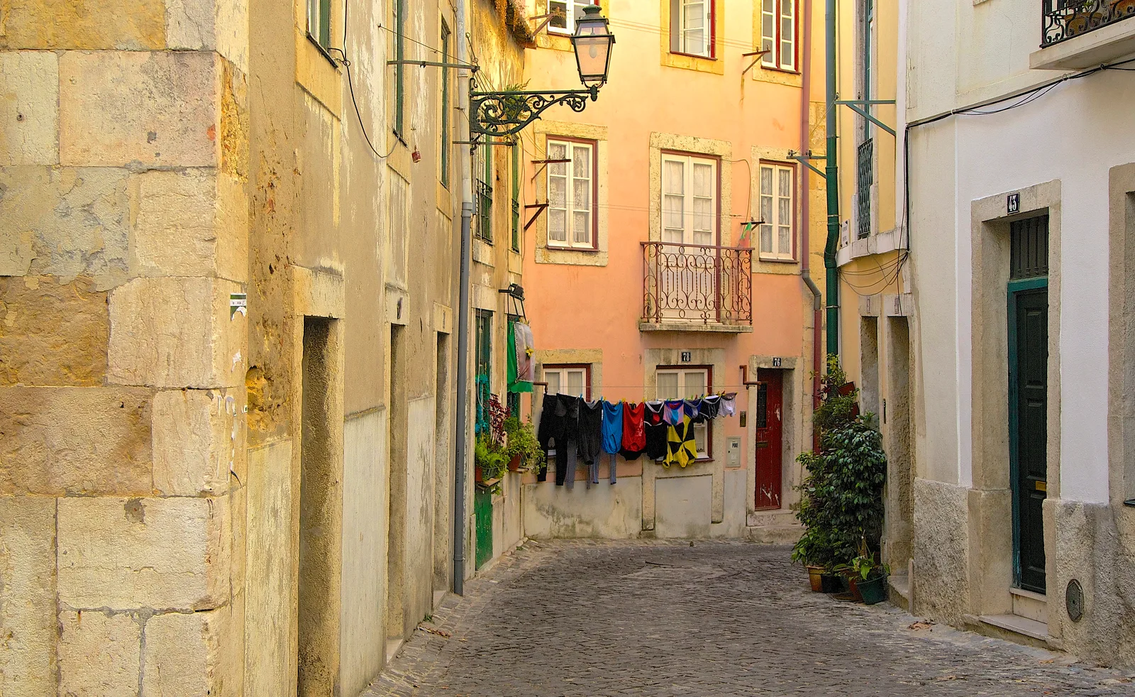 A steep cobbled alley with pastel houses and hanging washing in old Lisbon.