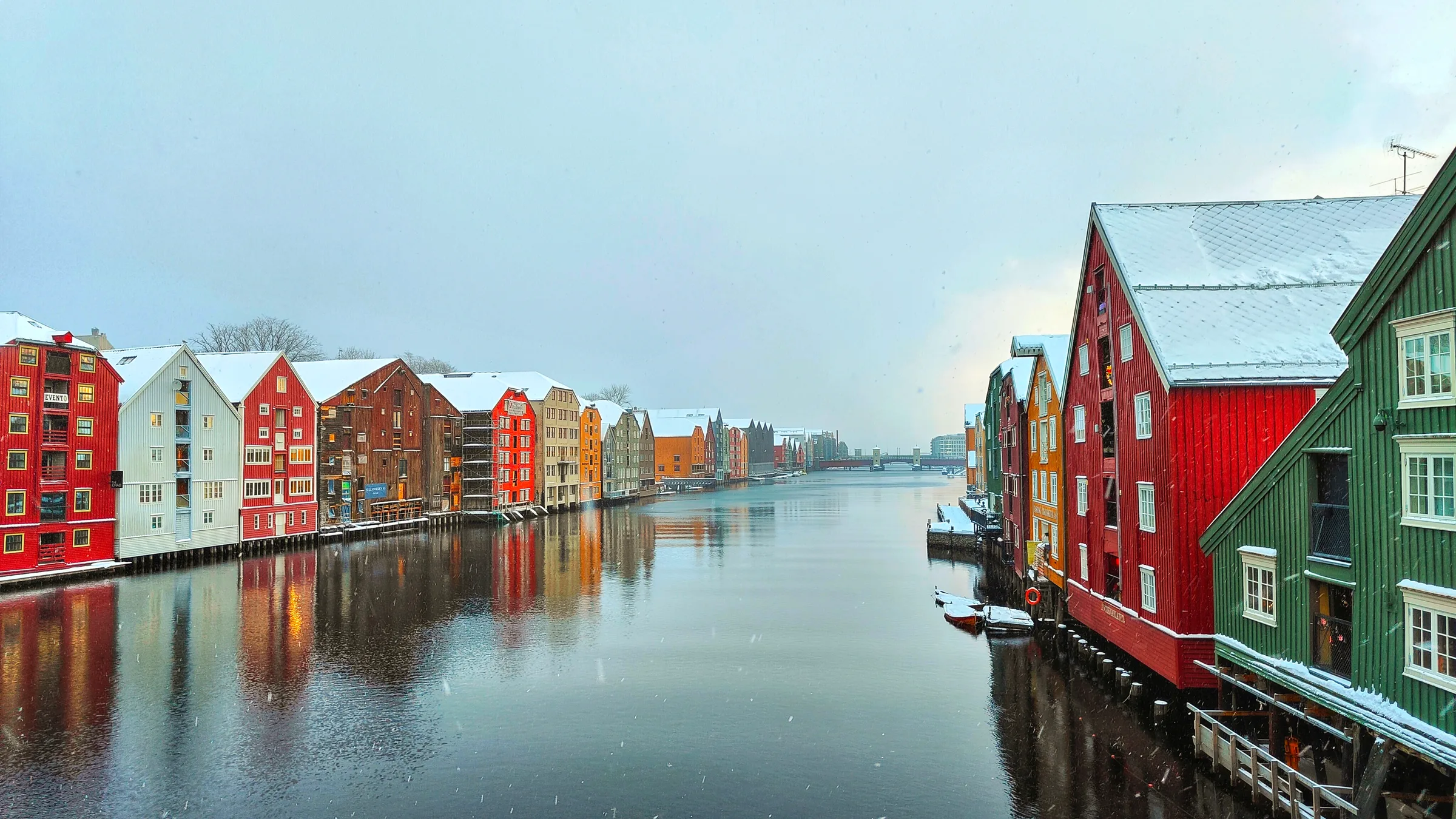 Brightly painted timber wharf warehouses on stilts along the Nidelva in Trondheim, dusted with early snow.