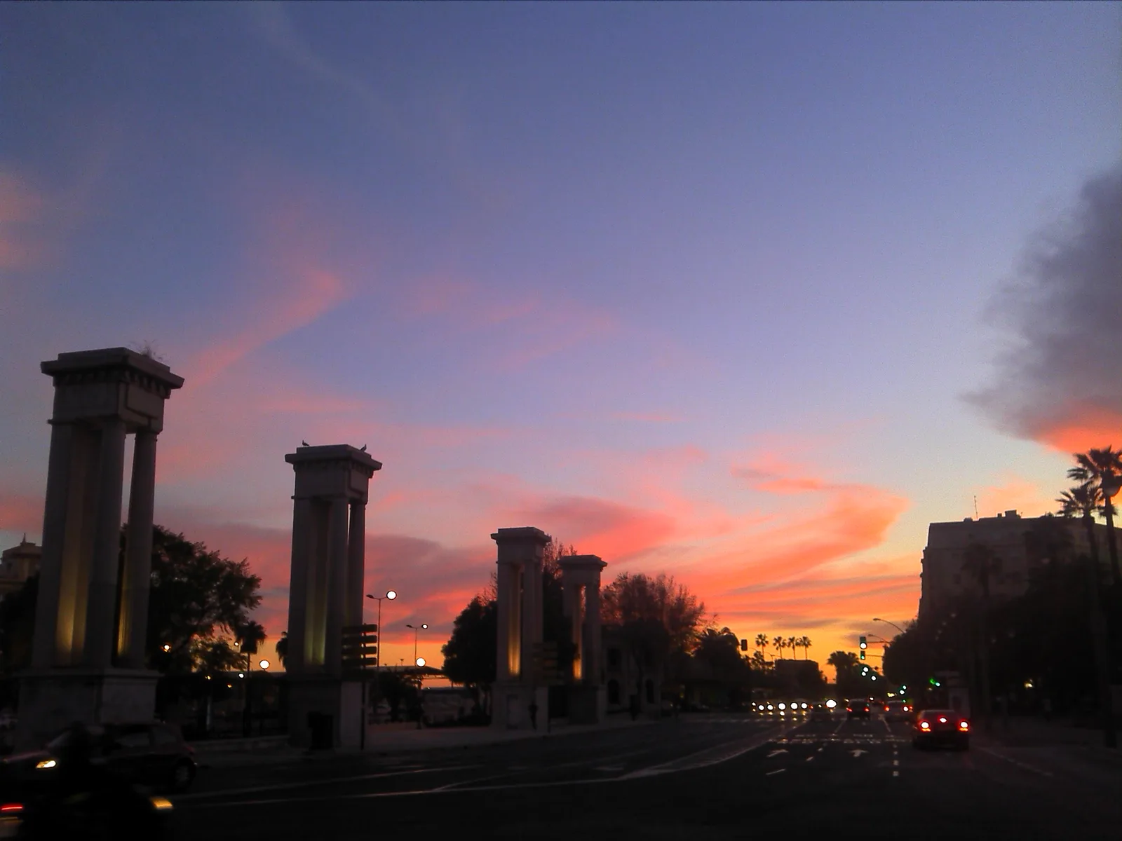 Stone pillars along the Málaga port avenue at sunset.