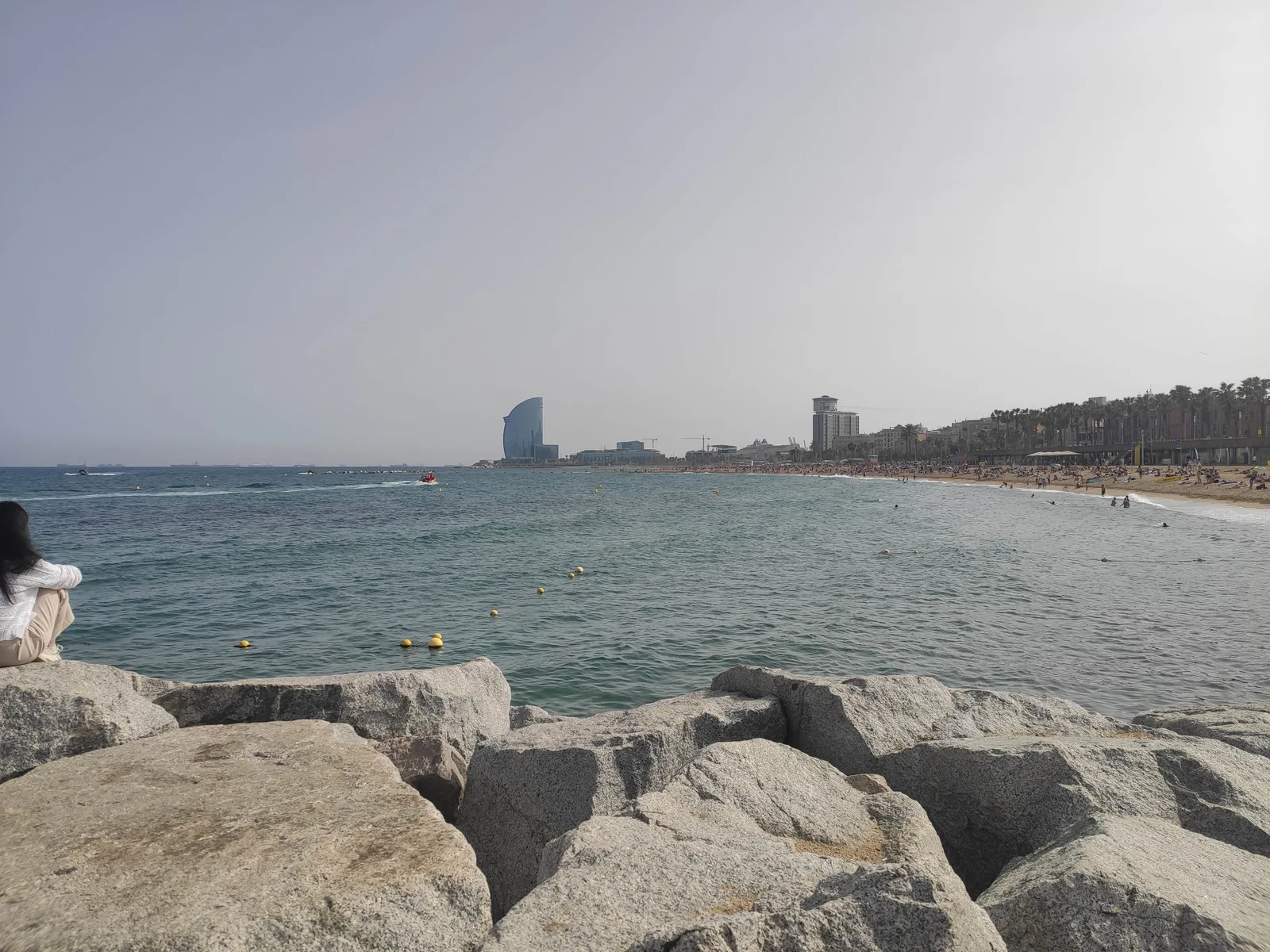 A wide view of Barceloneta Beach in Barcelona on a summer afternoon, waves rolling onto the sand