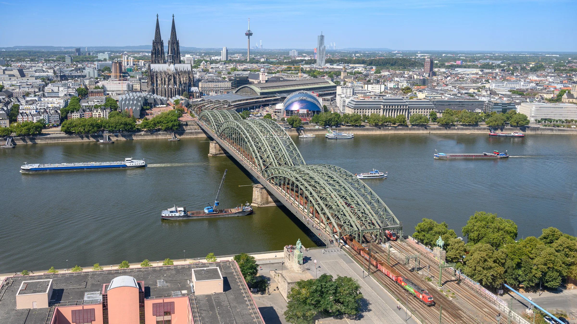 Elevated view of the Rhine at Cologne with the Hohenzollern Bridge, barges on the river and the cathedral spires on the skyline at left.