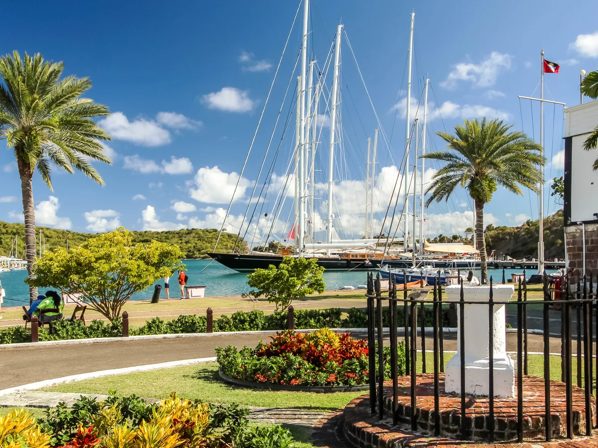 A green park, palm trees, flowering beds and the masts of moored yachts at Nelson's Dockyard, English Harbour.