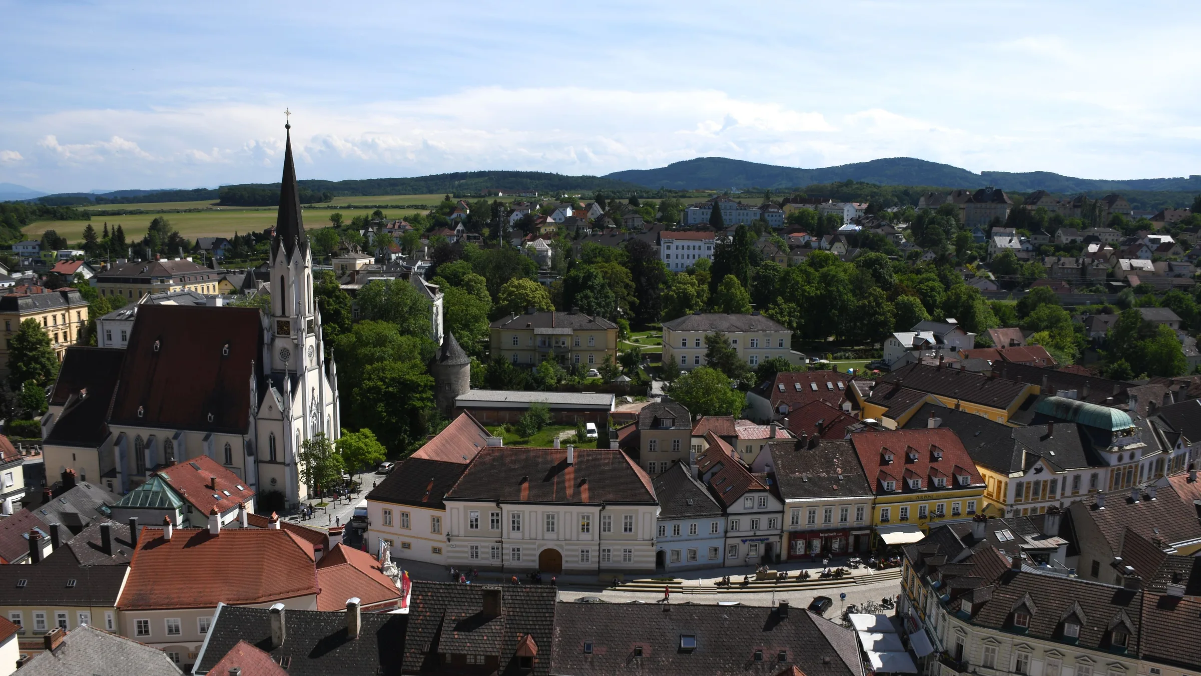 The rooftops of Melk town with the tall spire of the parish church and green hills beyond.