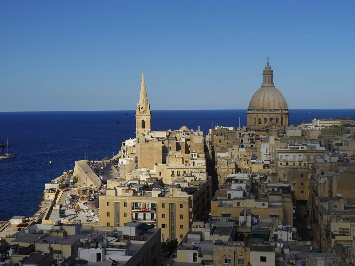 Rooftops of Valletta at dawn with the dome and spire against the sea.
