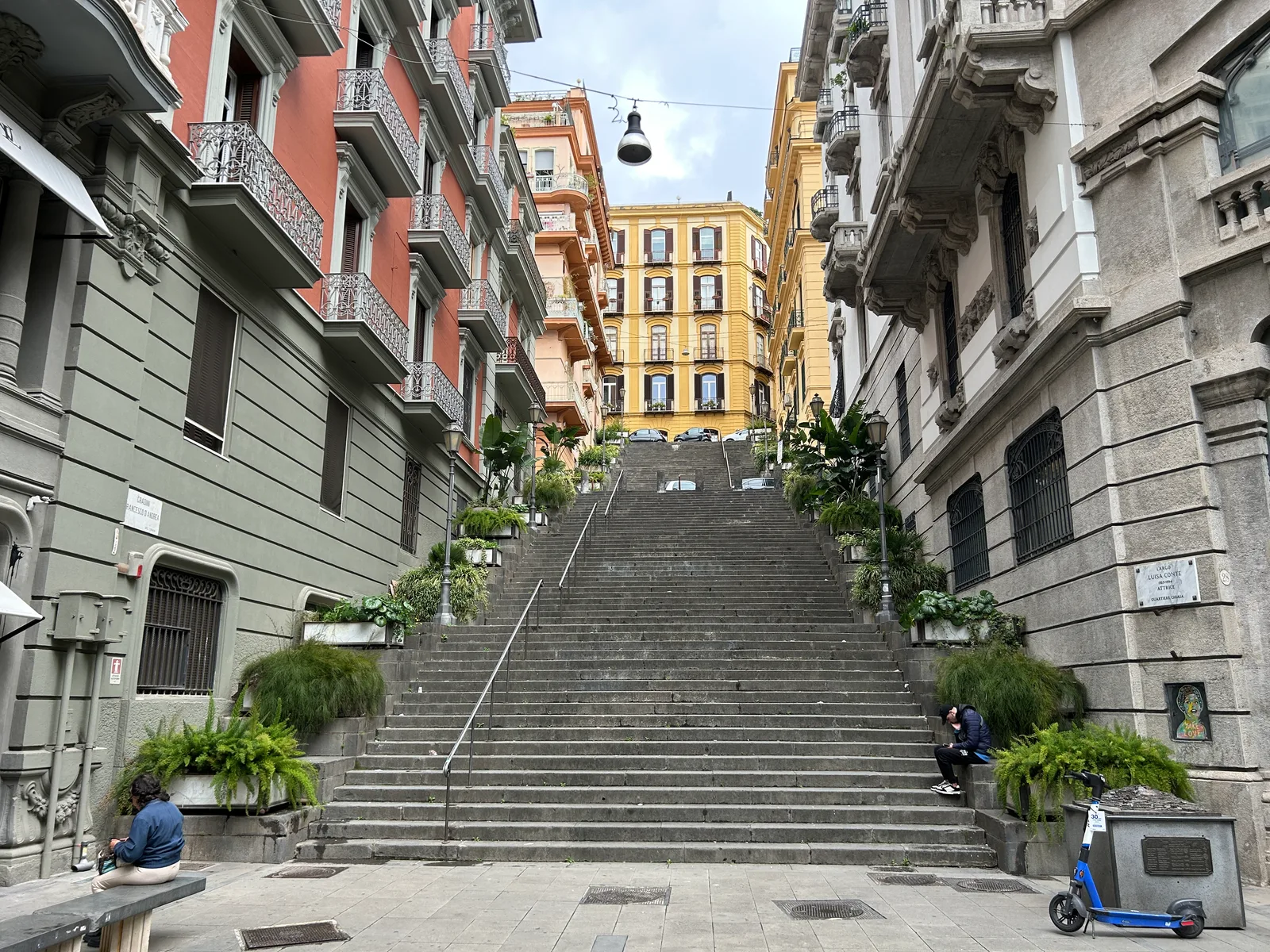 A wide stone staircase between tall apartment buildings in Naples with a scooter and a person on the steps.