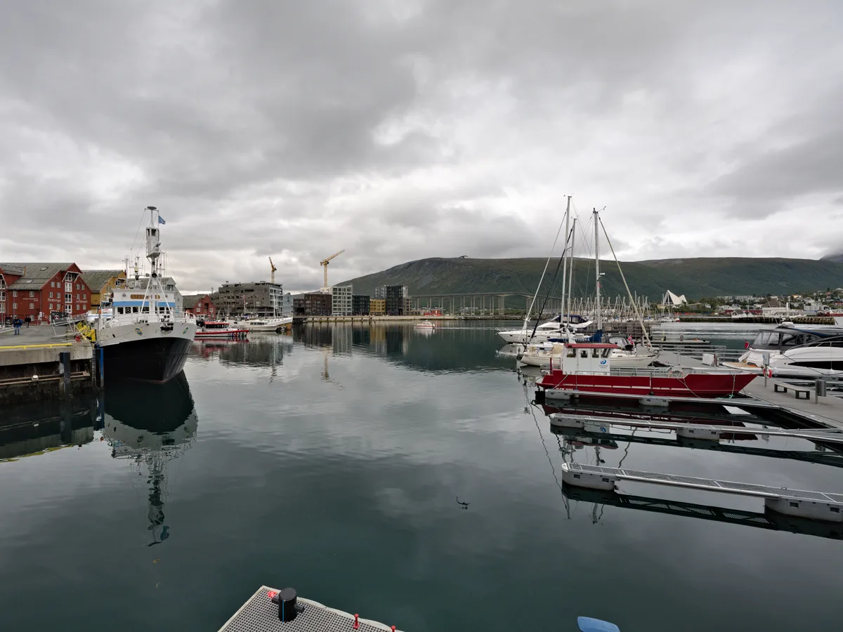 Calm water in the Tromso inner harbour at Indrehamna with a patrol vessel, marina yachts and cloud-reflected water.