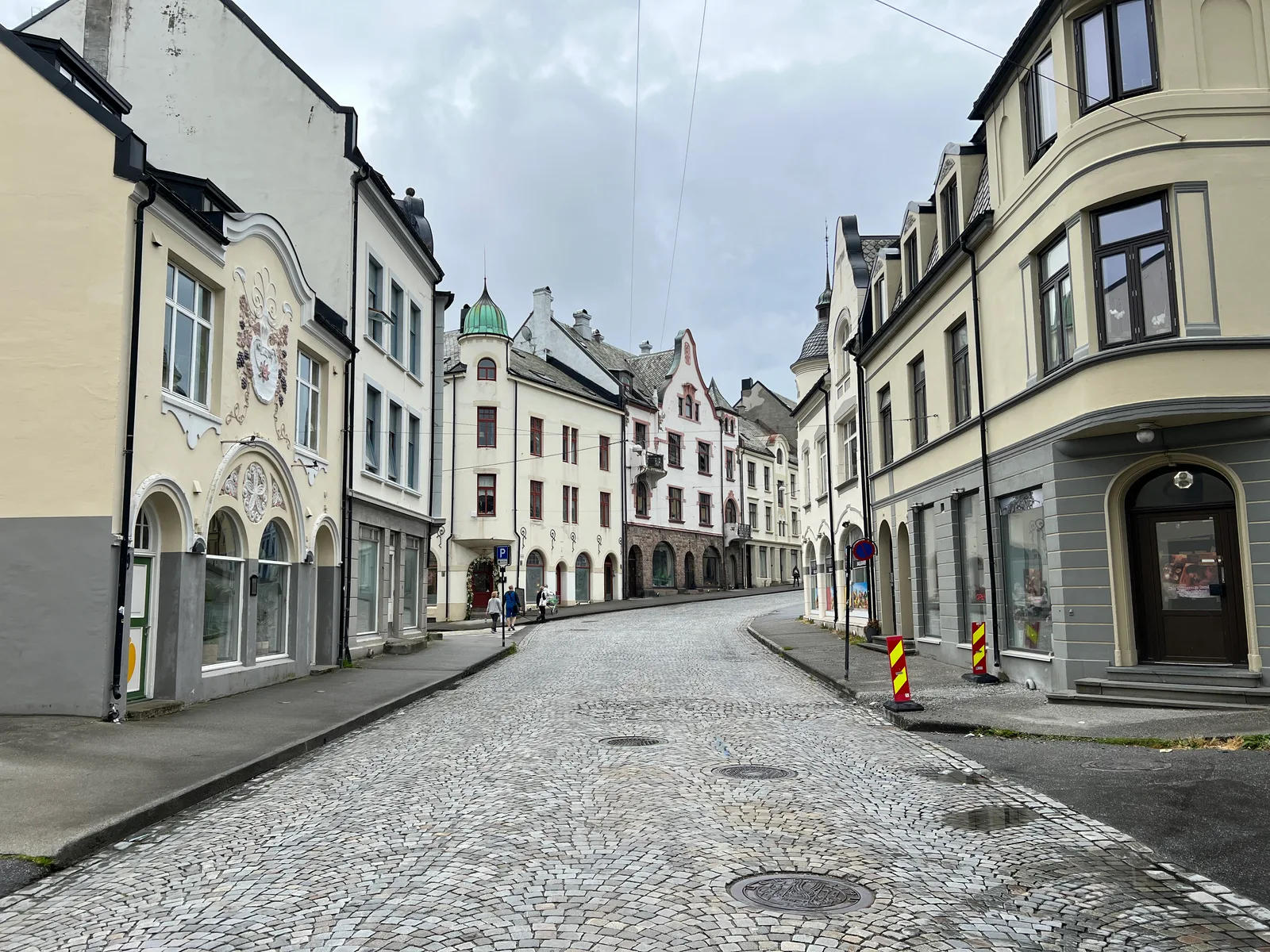 An empty cobbled Kirkegata in Alesund with Art Nouveau facades curving away under a grey sky.