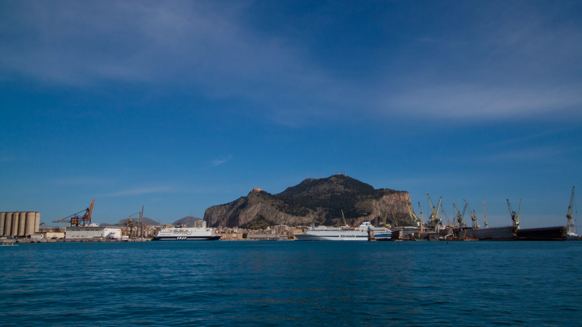 Palermo seen from the water of the gulf, with Monte Pellegrino rising behind the harbour cranes and ferries.