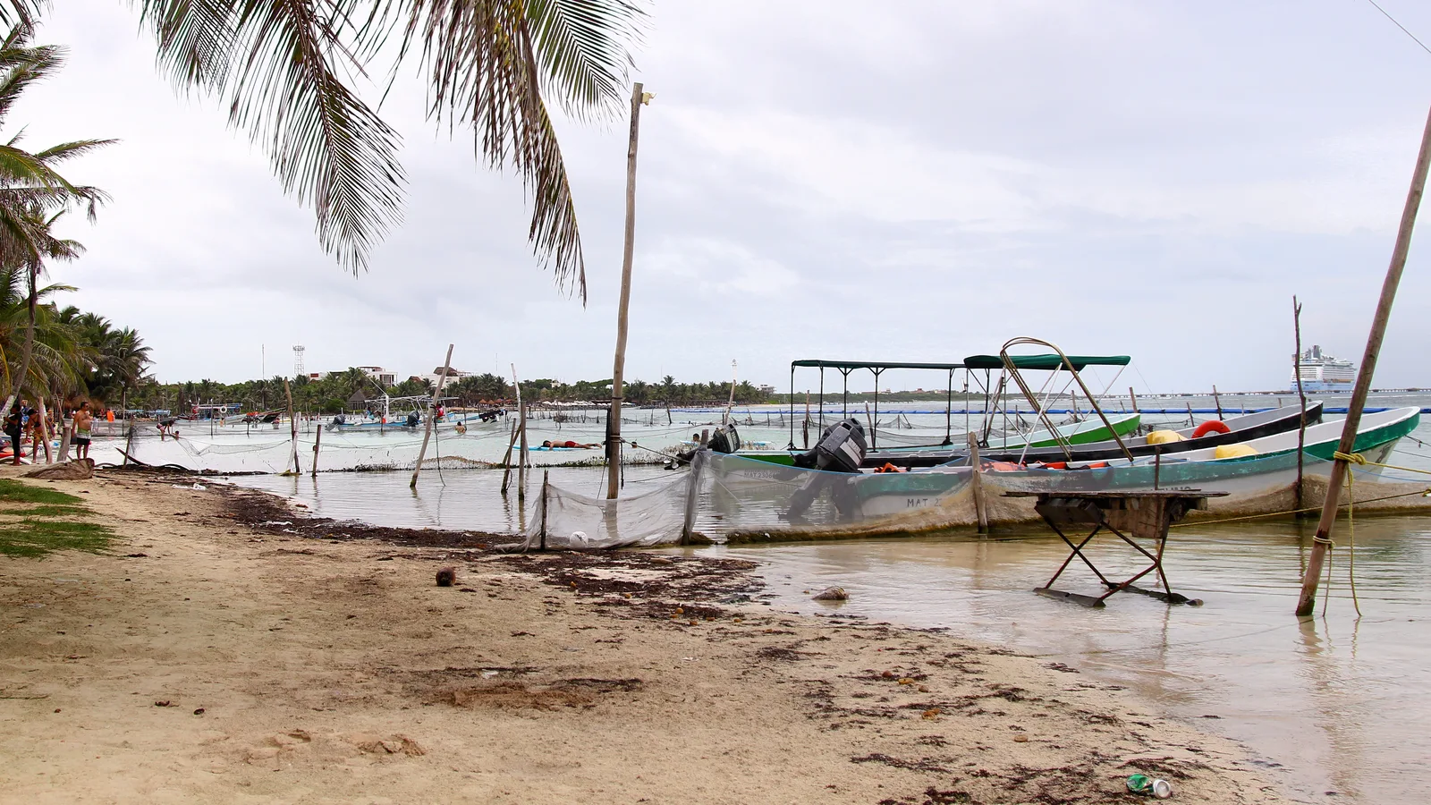 Small fishing boats beached on the shore at Mahahual under palm fronds.