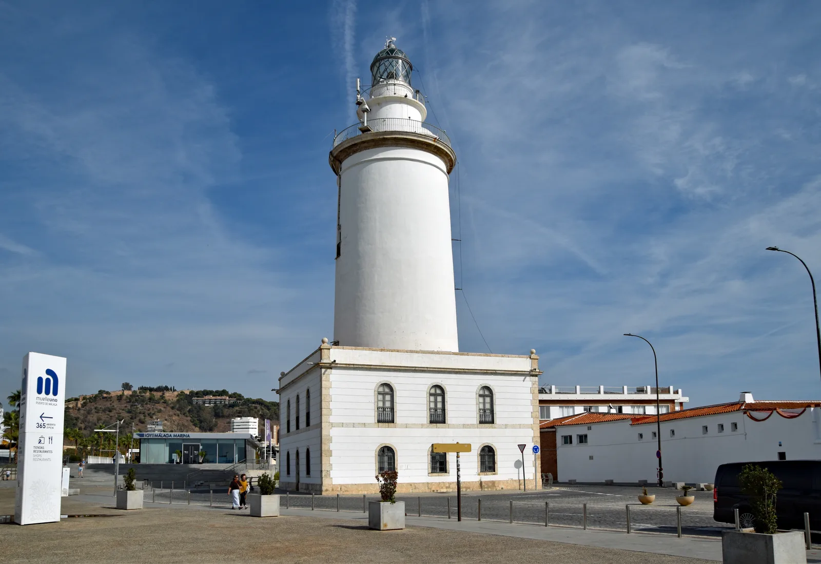 The white La Farola lighthouse at the port of Málaga under a streaky blue sky.