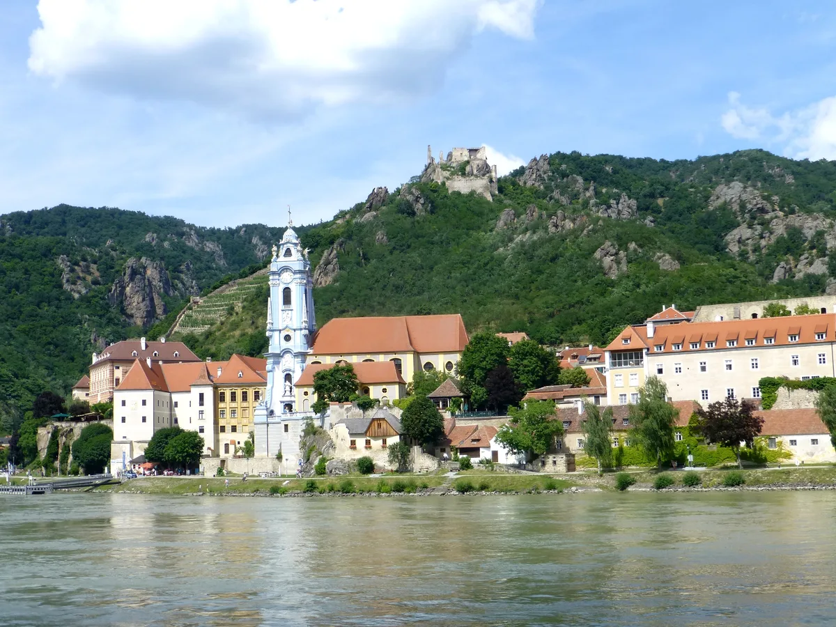 The blue baroque tower of Dürnstein Abbey and old town houses on the Danube bank below the ruined castle on the ridge.